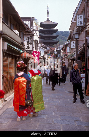 Zwei Touristen, die als Maiko (Geisha in Ausbildung) gekleidet sind, schlendern durch eine Seitenstraße in Kyoto mit Blick auf die Yasaka-Pagode, Japan. Stockfoto