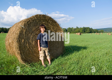 Junge mit Strohhalm in den Mund, so dass lustige Gesicht stützte sich auf Heuballen im Acker. Model Released Stockfoto