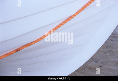 Detail von der Seite des Bogens eines weißen lackierten Bootes auf Sand oder Schlamm und mit einer orange Seil überqueren im Gegensatz Stockfoto