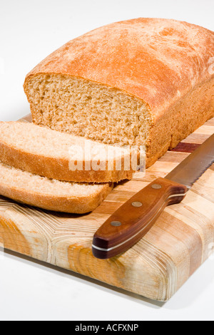 Ein Laib frisch gebackenem Vollkornbrot in Scheiben geschnitten auf einem Holz Schneidebrett mit einem Brotmesser Stockfoto