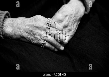 Hundert Jahre alte Damen-Hände halten einen Rosenkranz vor einem dunklen Hintergrund, Monochrom Stockfoto