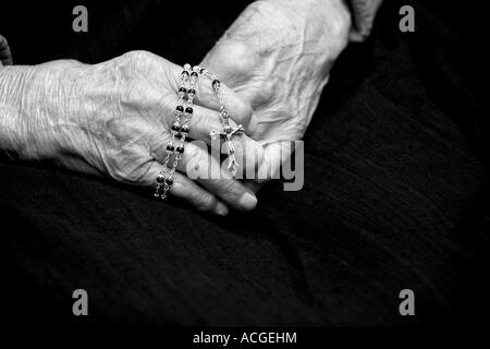 Hundert Jahre alte Damen-Hände halten einen Rosenkranz vor einem dunklen Hintergrund, Monochrom Stockfoto