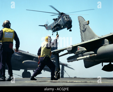 Flight Deck Officer startet Sea Harrier aus dem Flugdeck der HMS Ark Royal Sea King Mark 3 im Hintergrund. Stockfoto