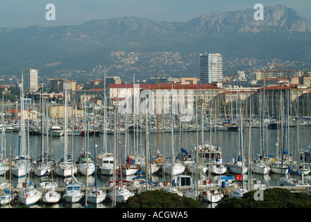 Teil des großen Marinehafens Toulon und Blick auf weitläufige Liegeplätze für kleine Boote und Masten mit Hintergrund einer hohen Felsbergkette an einem sonnigen Tag in Frankreich Stockfoto