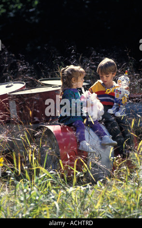 Zwei kaukasischen Kinder spielen auf Fässern von Industrieabfällen in einer Wiese Stockfoto