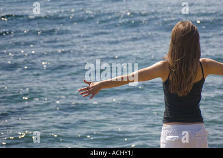 Frau weiße Hose schwarz Weste Top Sicht nach hinten von der Meer-Arme ausgestreckt in der Sonne Stockfoto