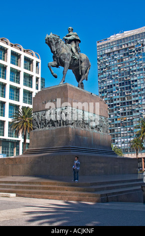 Plaza Independencia Independence Square mit dem Mausoleum von General Jose Artigas mit Reiterstandbild auf dem Platz. Allgemein auf ein Pferd... Eine Frau, die durch das imposante steinerne Denkmal stehen. Moderne Bürogebäude im Hintergrund. Montevideo, Uruguay, Südamerika Stockfoto