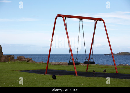 Roter Kinder schwingt in einem Spielplatz Park am Ufer in Portrush mit Tauben Stockfoto