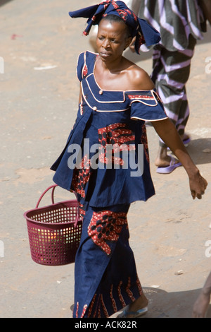 Frau in Tradional ab Schulter Kostüm und Kopf Schal zu Fuß mit Kunststoff Warenkorb Serekunda Markt Gambia Stockfoto