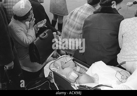 Ältere Mutter mit ihrem Baby in einem Kinderwagen, Frau, die ihr Make-up in der Öffentlichkeit, Handspiegel und Rauchen London 1970er UK HOMER SYKES Stockfoto