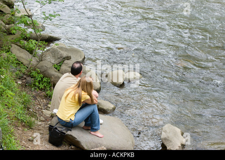 Junge Männer und Frauen sitzen friedlich auf Felsen am Ufer des Little Pigeon River in der Innenstadt von Gatlinburg, Tennessee, USA Stockfoto