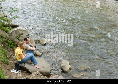 Junge Männer und Frauen sitzen friedlich auf Felsen am Ufer des Little Pigeon River in der Innenstadt von Gatlinburg, Tennessee, USA Stockfoto