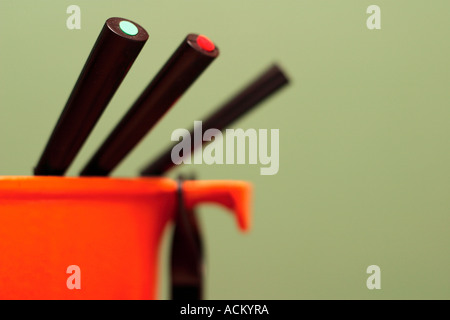 Orange Fondue Teller mit farbcodierten Zinken vor einem grünen Hintergrund. Stockfoto