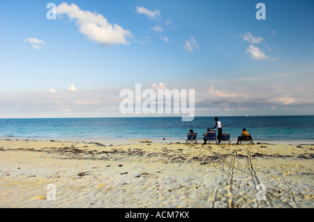 Gruppe von Menschen sitzen auf Sandstrand azurblauen Meer blauer Himmel weiße Wolken Küstenlinie Stockfoto