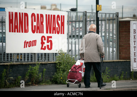 Ältere Mann schieben Einkaufswagen vorbei an einer Auto-Waschanlagen-Werbeschild, England UK Stockfoto