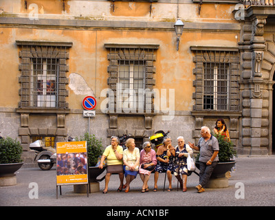 Fünf Frauen sitzen auf einer Bank in der Piazza hören zu einem Mann sagen, eine Geschichte in Orvieto Itay als eine junge Frau aus Behi blickt auf Stockfoto
