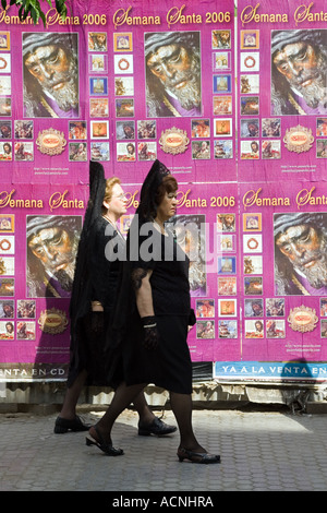 Frauen gekleidet mit traditionellen Mantilla zu Fuß vor einer Wand bedeckt mit religiösen Plakate, Karwoche, Sevilla, 2006 Stockfoto