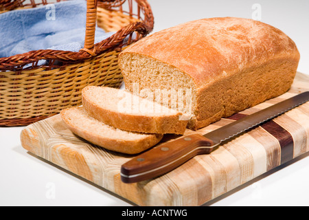 Ein Laib frisch gebackenem Vollkornbrot in Scheiben geschnitten auf einem Holz Schneidebrett mit einem Brotmesser bereit, in einen Brotkorb Stockfoto