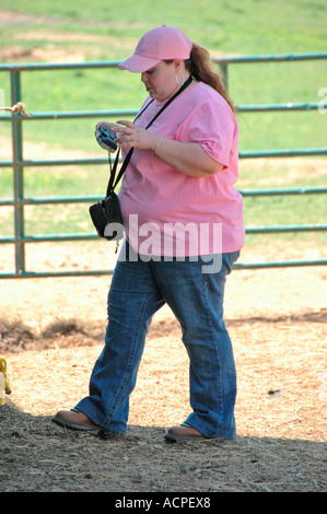 Sehr große Frau auf Zaun auf dude Ranch in der Land beobachten Vieh Roundup von Cowboys mit einer Kamera Stockfoto