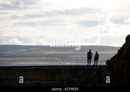 zwei Jungs im Teenageralter in Neoprenanzüge stehen auf Hafenmauer Blick in das Wasser mit Grafschaft Donegal im Hintergrund Stockfoto