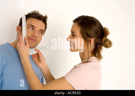Frau, messen das Gesicht des Mannes mit Lineal, lächelnd, Nahaufnahme Stockfoto
