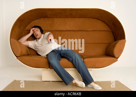 Junger Mann auf Sofa, tragen von Kopfhörern und Fernbedienung halten Stockfoto