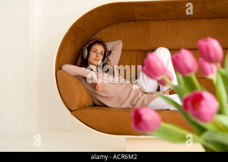 Junge Frau lag auf Sofa, tragen von Kopfhörern Stockfoto