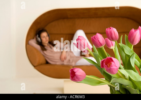 Entspannen Sie sich auf Sofa, junge Frau konzentrieren sich auf Tulpen im Vordergrund Stockfoto