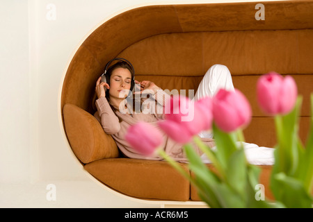 Entspannen Sie sich auf Sofa mit Kopfhörer, Frau Rosa Tulpen im Vordergrund Stockfoto