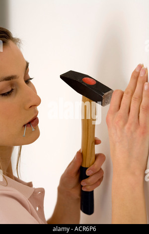 Junge Frau Nagel in Wand klopfen, mit Hammer, Nahaufnahme Stockfoto