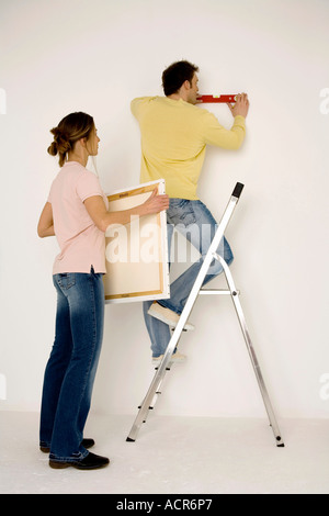 Junges Paar aufhängen, Malerei, Mann steht auf Leiter Stockfoto