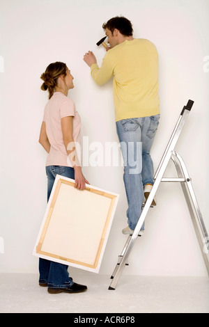 Junges Paar aufhängen, Malerei, Mann steht auf Leiter Stockfoto