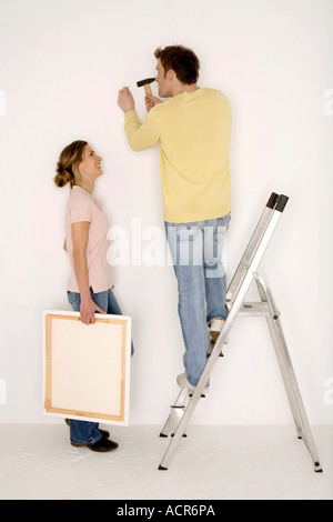 Junges Paar, Mann Hämmern Nagel in Wand Stockfoto