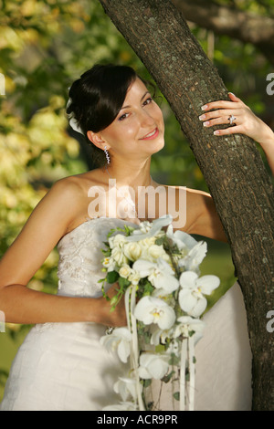 Porträt einer Braut stand neben einem Baum mit Blumenstrauß Stockfoto