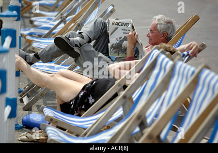 Ein Mann liest die Zeitung "Racing Post" sitzend in einem Liegestuhl am Meer bei Weymouth UK Stockfoto