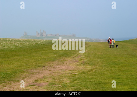 ein Ehepaar im Ruhestand zu Fuß ihren Hund in der Nähe von Dunstanburgh Castle, die durch den Nebel im Hintergrund zu sehen ist Stockfoto