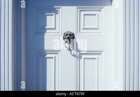 Stilvolle getäfelten Haustür und gerippten Pfosten mit angeschlagenen Kupfer Löwen Kopf Klopfer wirft Schatten frisch weiß gestrichen Stockfoto