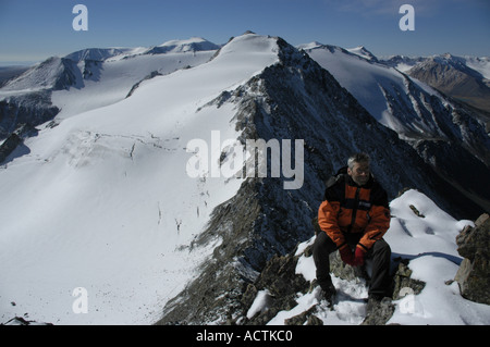 Herr Bergsteiger sitzt auf den Felsen vor einem schneebedeckten Berg Kharkhiraa mongolischen Altai in der Nähe von Ulaangom Uvs Aymag Mongolei Stockfoto