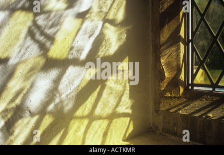 Projektion von klaren kleinen handgefertigten Platz oder Diamant verbleit Glasscheiben auf Creme lackiert rauhe Wand Fenster in warmes Licht Stockfoto