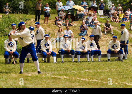 BASEBALL SCHLAGMANN SOLL SCHWINGEN SEINE SCHLÄGER UM DEN BALL ZU SCHLAGEN, WÄHREND SEINE TEAMKOLLEGEN UND ZUSCHAUER BEOBACHTEN Stockfoto