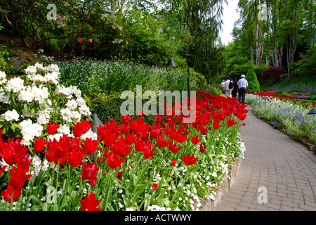 LANDSCAPE VIEW OF THREE PERSONS WALKING IN THE BEAUTIFUL GARDEN OF TULIPS AND OTHER FLOWERS Stockfoto
