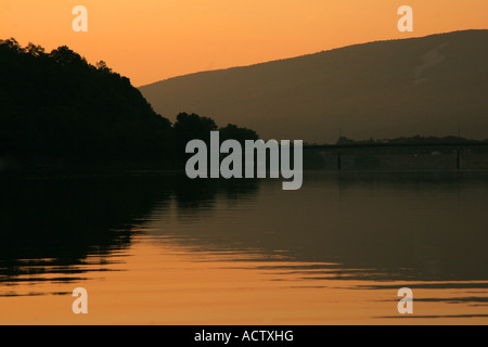 Leuchtend orange Sonnenaufgang über dem Fluss mit Bäumen und Hügeln widerspiegelt. Stockfoto