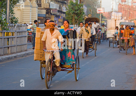 Straßenszene entlang Chandni Chowk mit einer Fahrradrikscha und Passagiere im Vordergrund und das Rote Fort (Lal Qila) hinter. Stockfoto