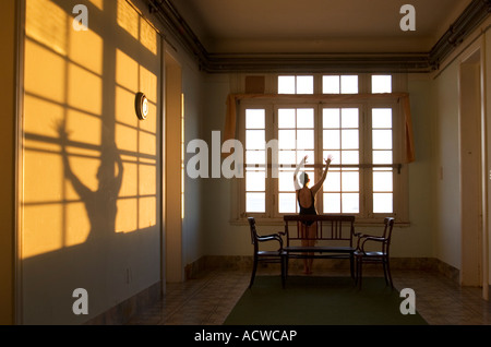 Frau, die durch ein Fenster mit langen Schatten bei Sonnenuntergang Stockfoto