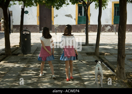 Zwillingsmädchen, die ihren Hund in einer Reihe von Orangenbäumen in der Real Alcazar Palast Sevilla, Andalusien, Südspanien Stockfoto