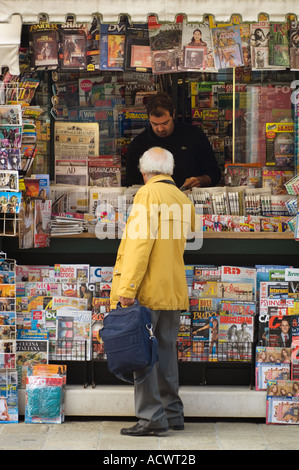 Älterer Mann in eine gelbe Regenjacke Kauf etwas an einem Zeitungskiosk in Venedig Italien Stockfoto