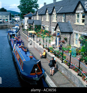 Boote, die von einer Reihe von Reihenhäusern vertäut sind, und Touristen, die auf dem Monmouthshire und dem Brecon Canal Powys Wales UK KATHY DEWITT vorbeilaufen Stockfoto