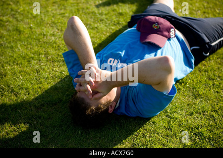 Mann liegt auf dem Rasen mit seinem Kopf in seine Hände nach einem Spiel suchen Sie erschöpft und müde, UK Stockfoto