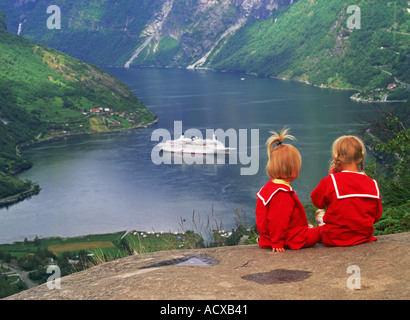 Schwestern in roten Kleidern sitzen über dem Geirangerfjord mit Passagier Kreuzfahrtschiff in Nord-Norwegen Stockfoto