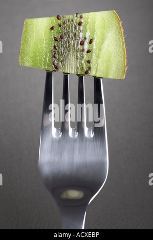 Scheibe eine Kiwi - Actinidia Deliciosa stecken auf einer Gabel auf einem grauen Hintergrund Stockfoto